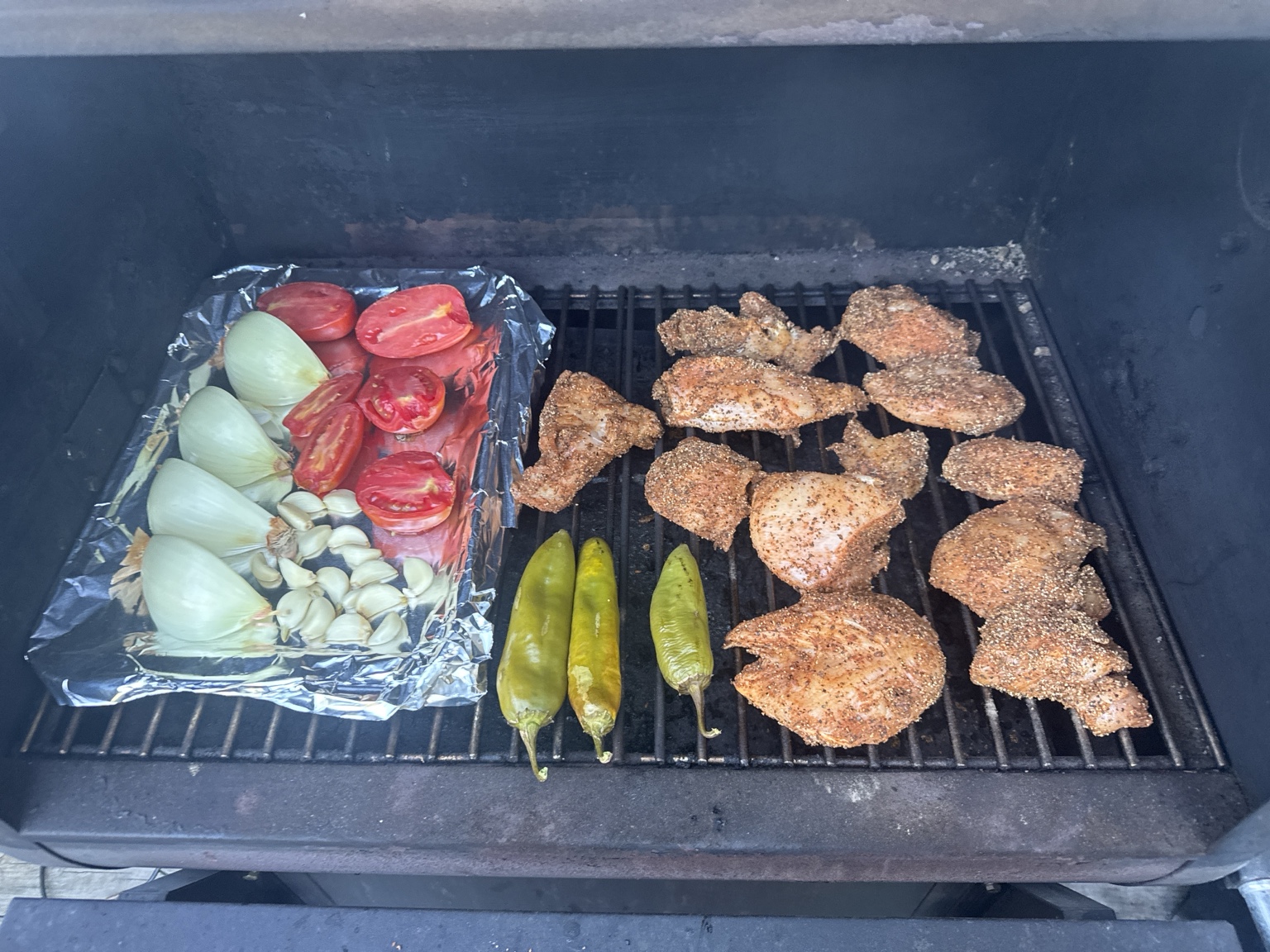 Seasoned chicken, tomatoes, onions, garlic and Anaheim peppers cooking on the smoker