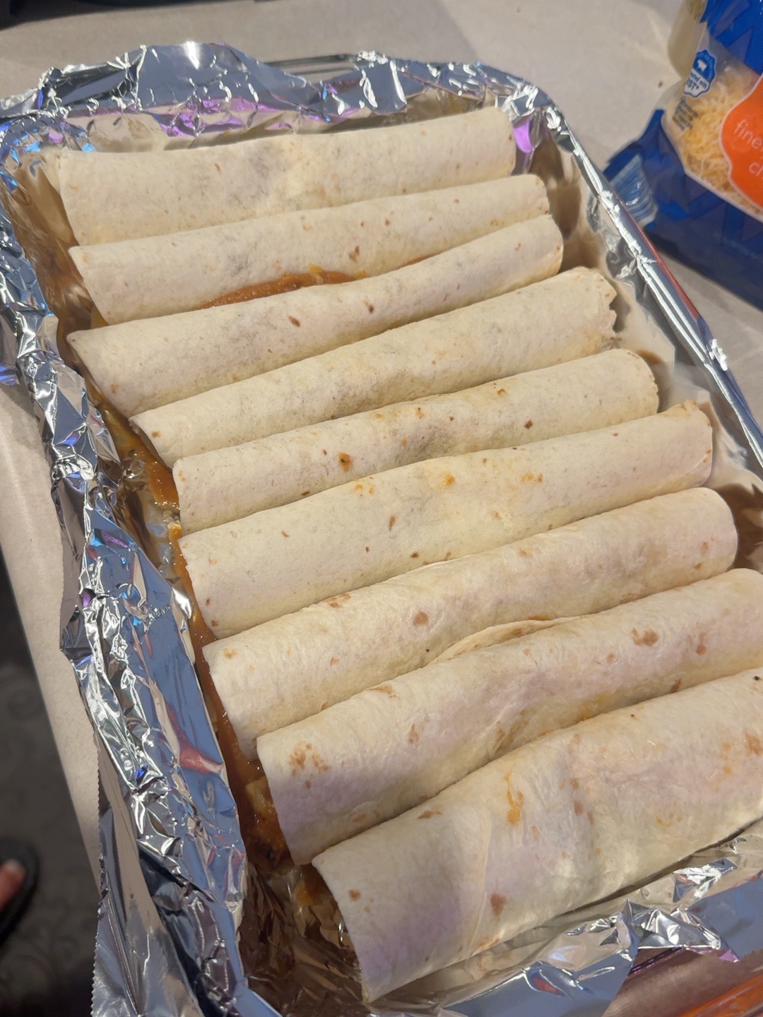 Rolled chicken enchiladas arranged in a baking pan