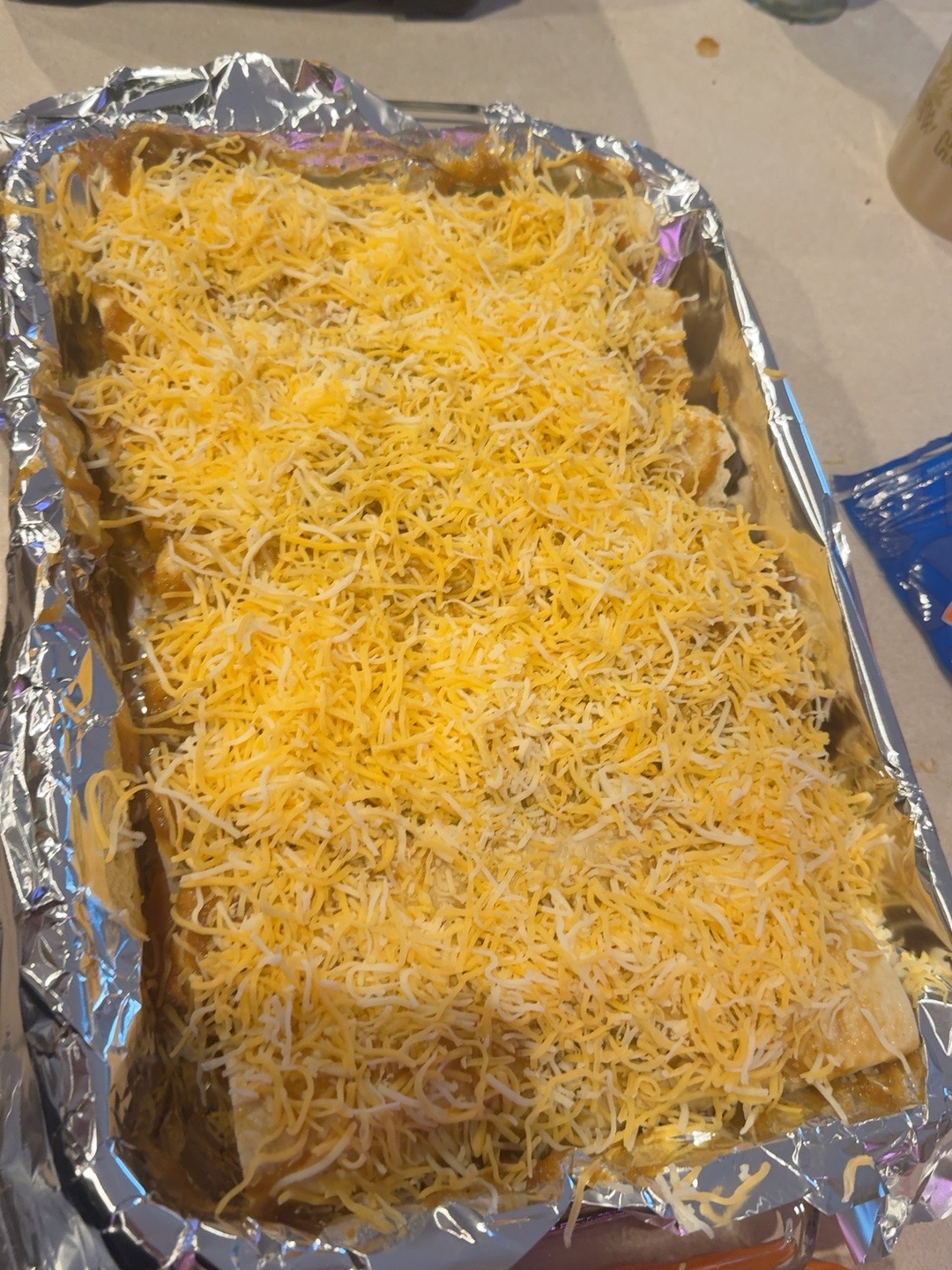 Smoked chicken enchiladas covered with shredded cheese before baking