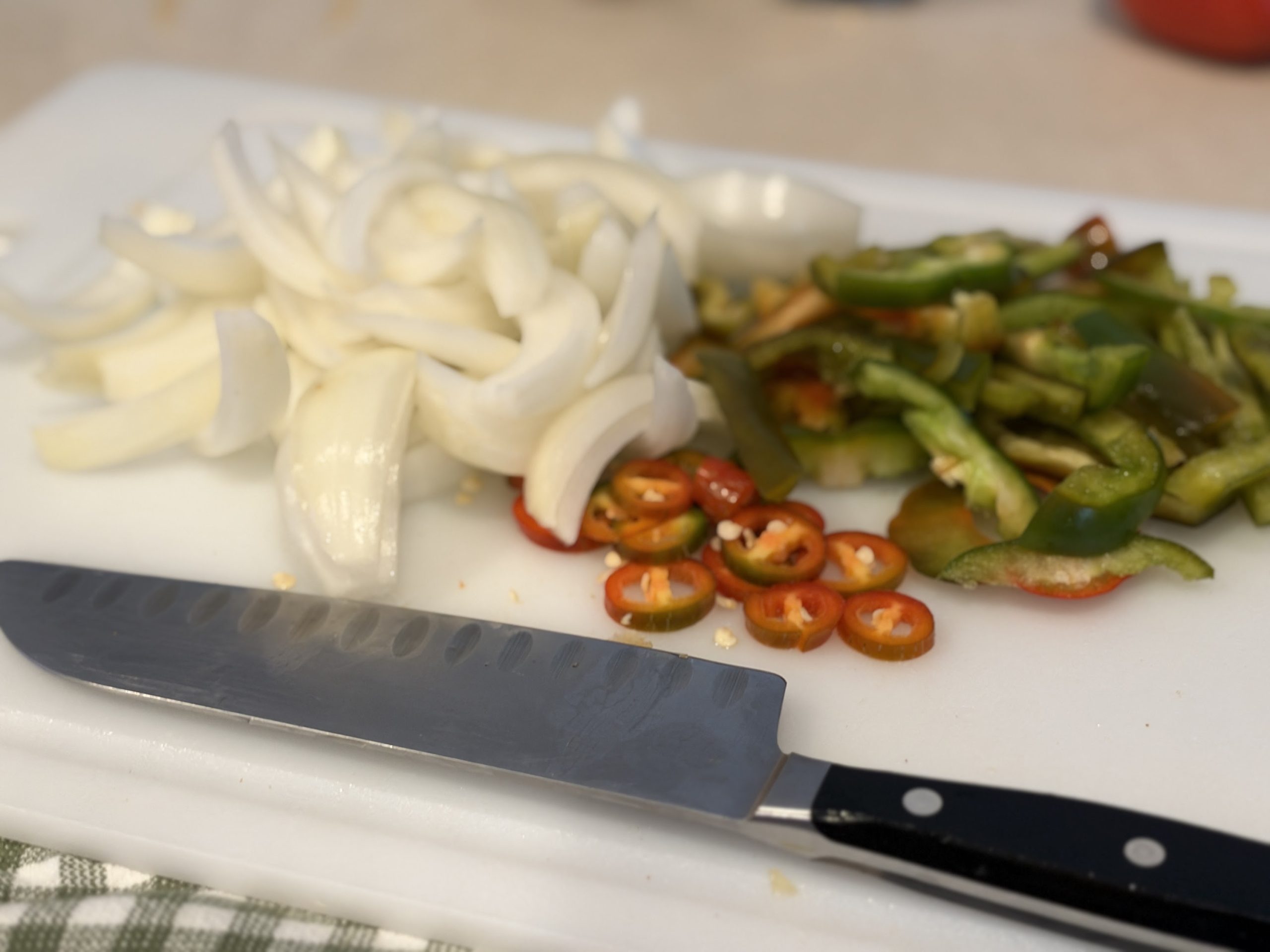 Sliced onion, bell pepper and red jalapeño on a cutting board with chef’s knife