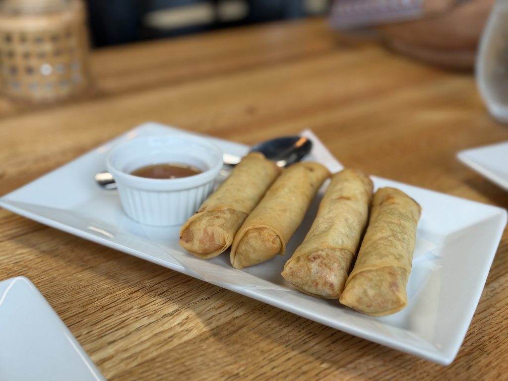 Four crispy chicken egg rolls with dipping sauce at Hoang Khao