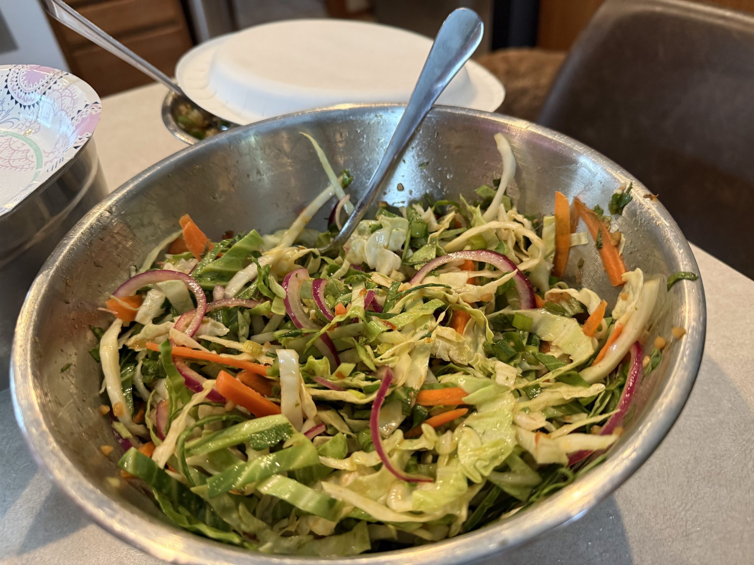 Fresh Asian-style cabbage slaw with carrots, red onion and green vegetables in a metal bowl.