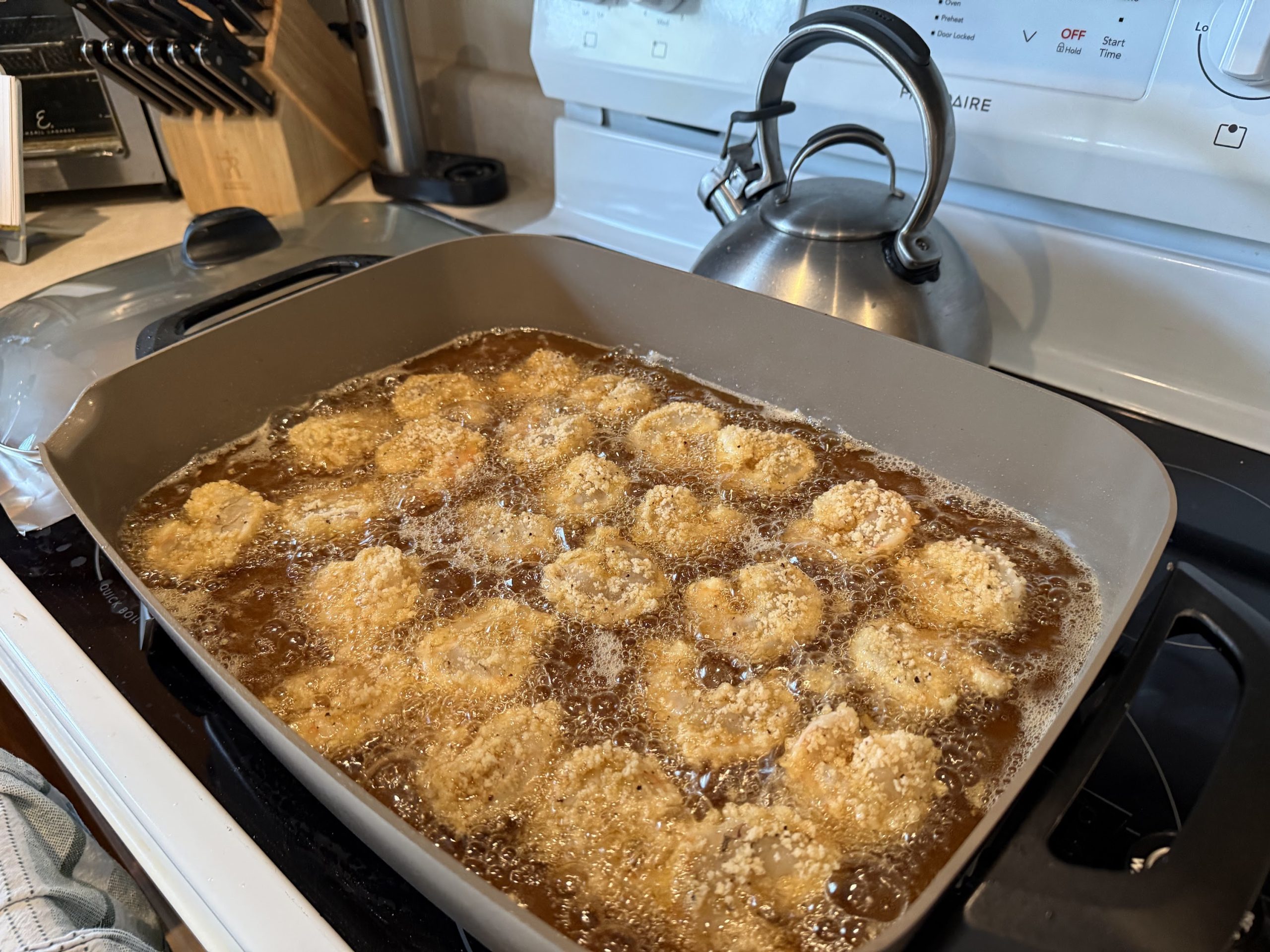 Breaded shrimp frying in hot oil in a large skillet in K&K Kitchen.