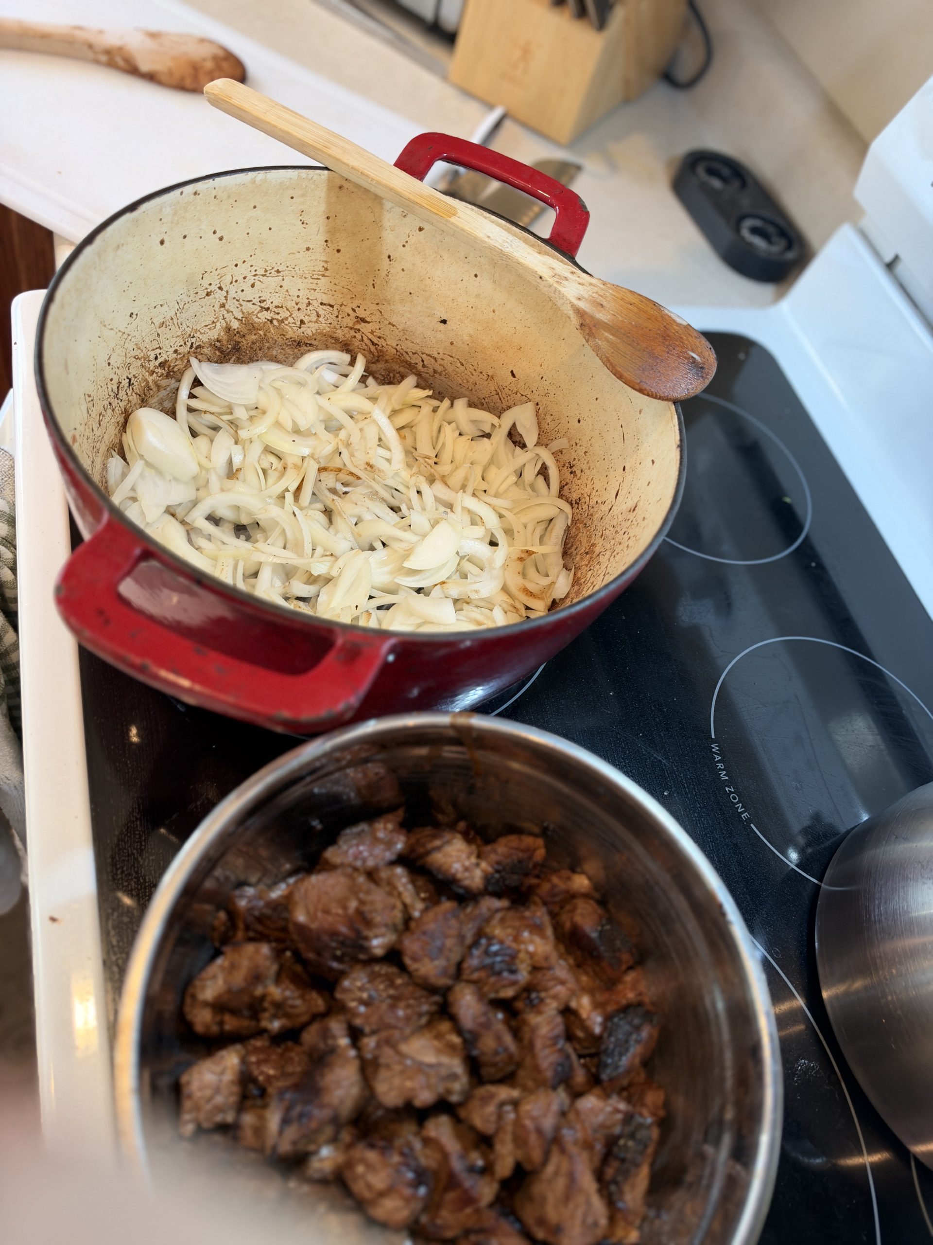 Sliced onions cooking in the Dutch oven beside the browned beef
