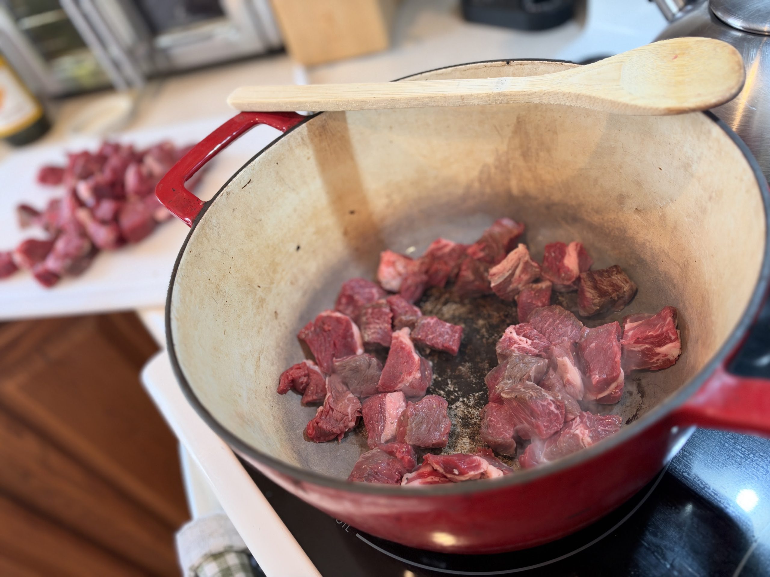 Chunks of chuck roast browning in a red Dutch oven