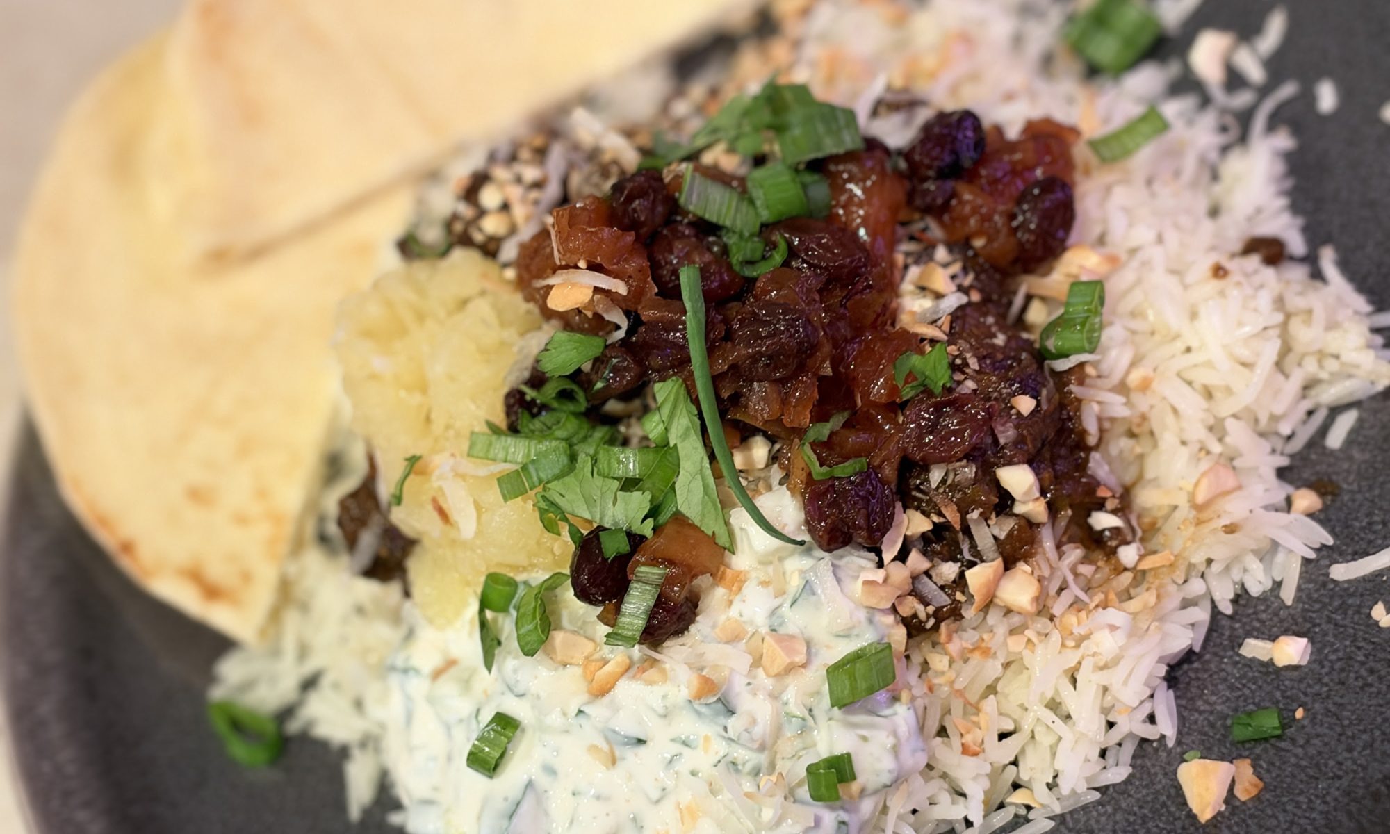 Tender beef curry over saffron basmati rice with apple-raisin chutney, raita, coconut, herbs and naan