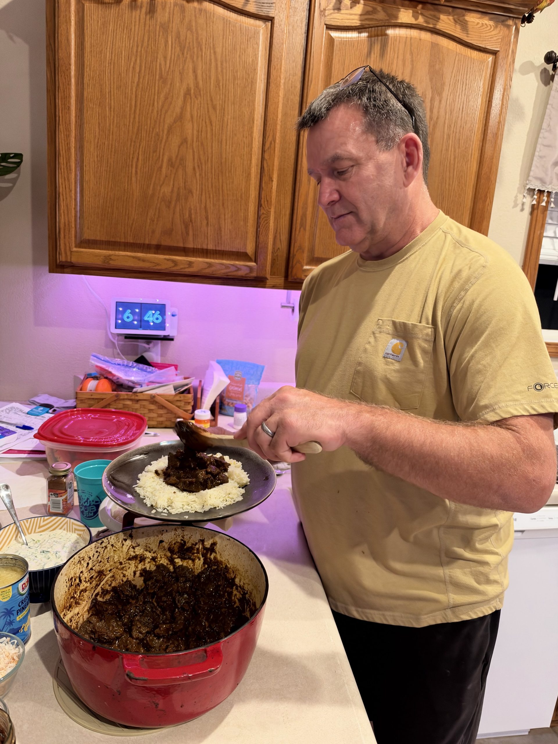 Kirk spooning beef curry onto a plate of rice at the kitchen counter